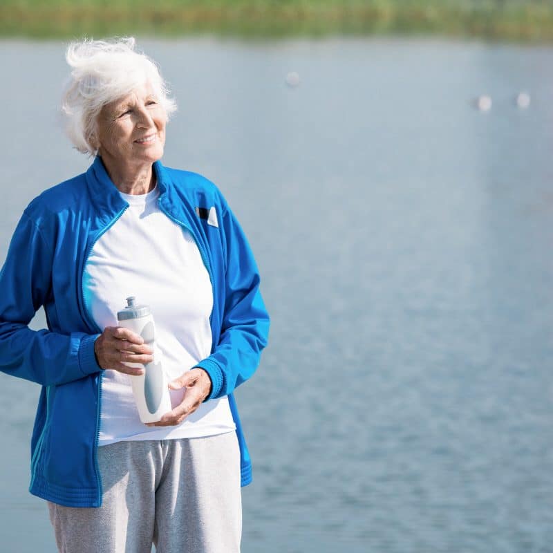Waist up portrait of active senior woman looking away  and holding water bottle while enjoying morning run in park, copy space